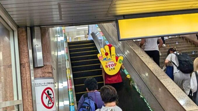 Miembro de la patrulla civil con cartel en la espalda, fomentando la campaña para que los usuarios permanezcan detenidos en escaleras eléctricas.